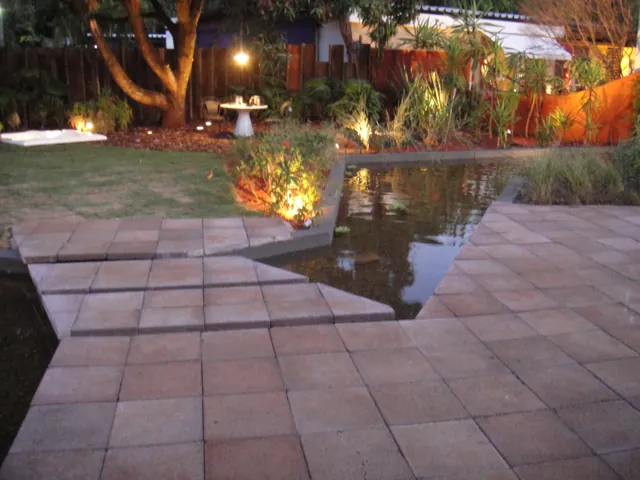 Caminho de Drenatu sobre o espelho d'água, com jardim iluminado